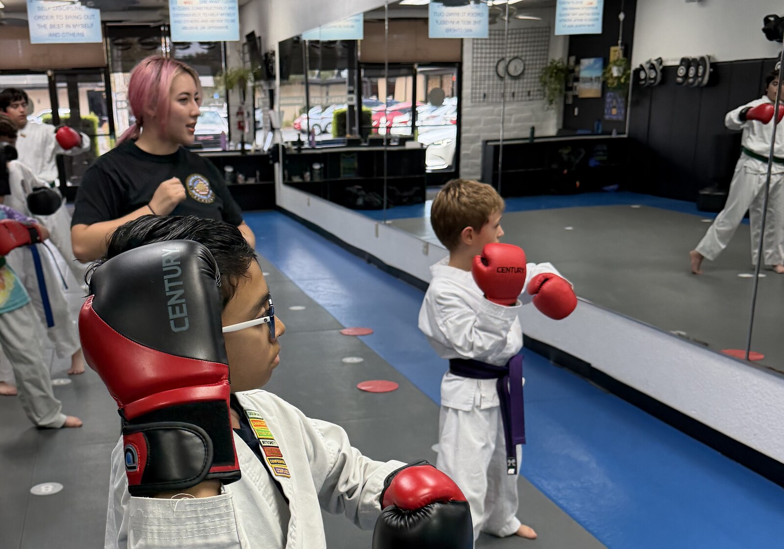 Students in white gis with colored belts and boxing gloves holding guard stances on the mats while an instructor demonstrates at Livermore Martial Arts Academy